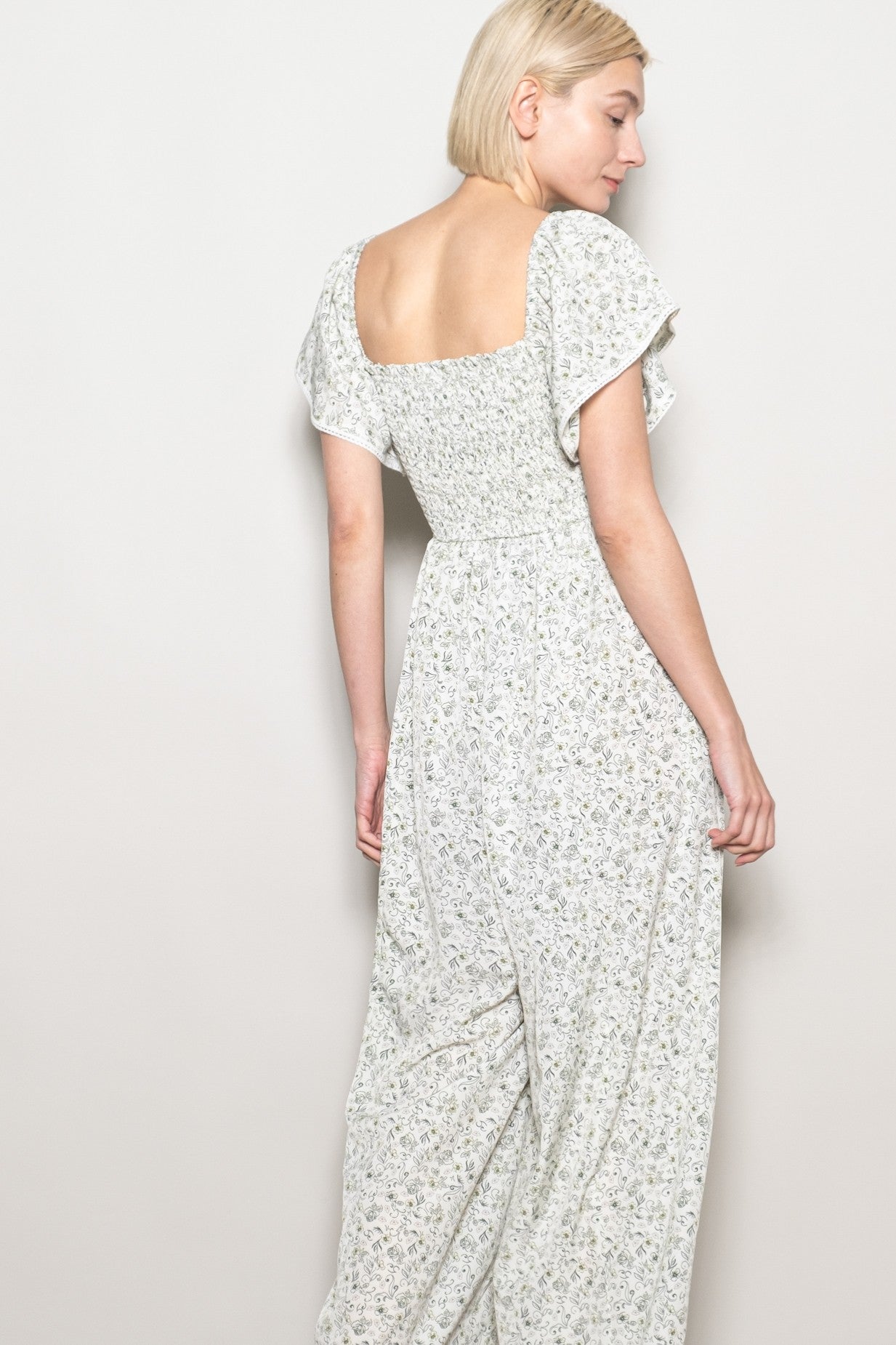 woman wearing a back view of a floral print maxi dress with a square neckline and short flutter sleeves