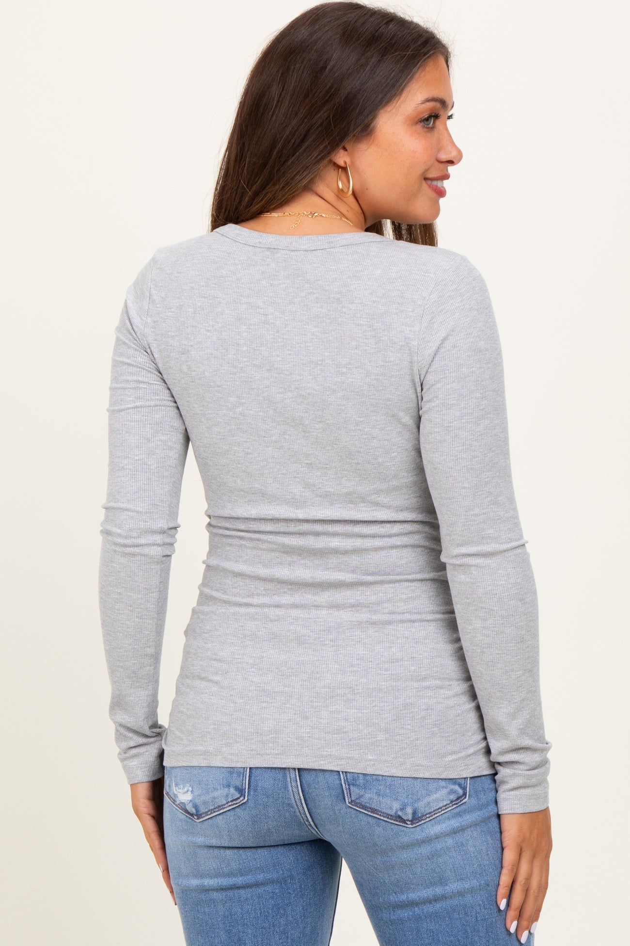 woman wearing a fitted gray long sleeve maternity top seen from the back, paired with blue jeans