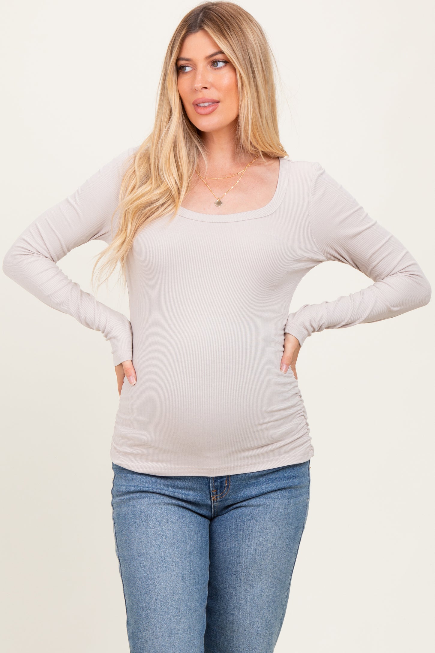 woman wearing a light beige long sleeve ribbed maternity top and showcasing her baby bump
