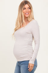 woman wearing a light taupe long sleeve maternity top, showing her baby bump, paired with light blue jeans