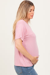 woman wearing a light pink short sleeve maternity top and holding her baby bump