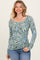 woman wearing a green floral long sleeve henley top with buttons and a scoop neckline, paired with blue jeans