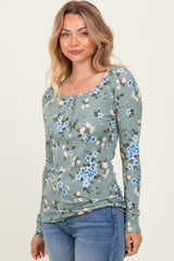 woman wearing a green floral long sleeve top with a square neckline and button details paired with blue jeans