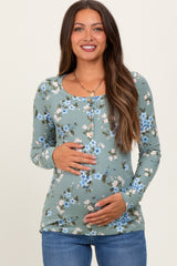 woman wearing a green floral maternity top with long sleeves and a rounded neckline, cradling her baby bump