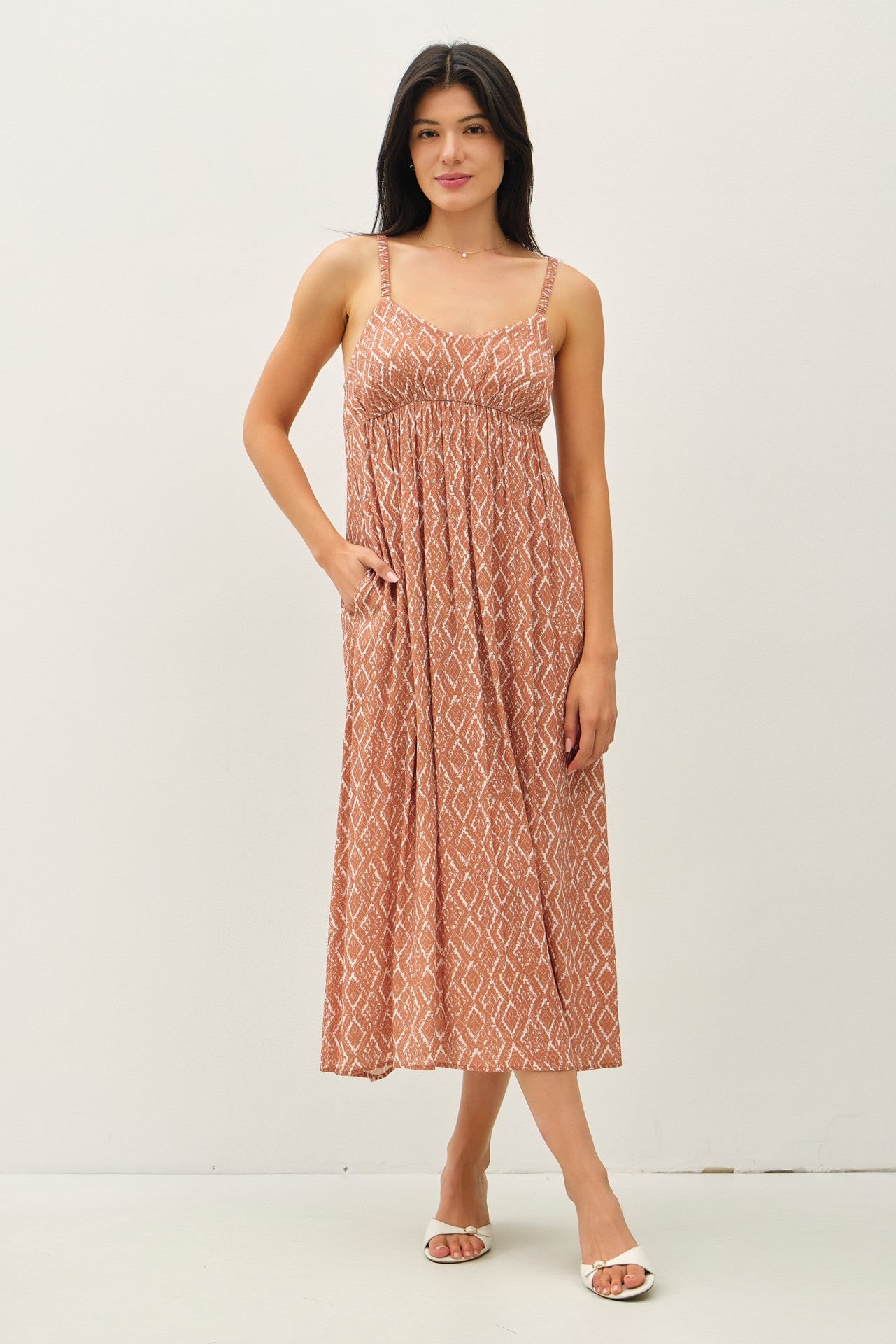 woman wearing a rust-colored patterned maxi dress with adjustable straps and pockets