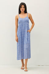 woman wearing a blue patterned sundress with thin straps and pockets, standing against a plain background