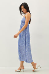 woman wearing a blue patterned maxi dress with spaghetti straps and a tiered design, walking against a plain background