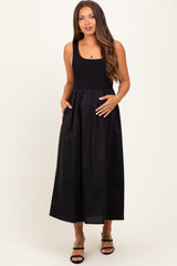 woman wearing a black maternity maxi dress with pockets and a fitted bodice, gently holding her baby bump