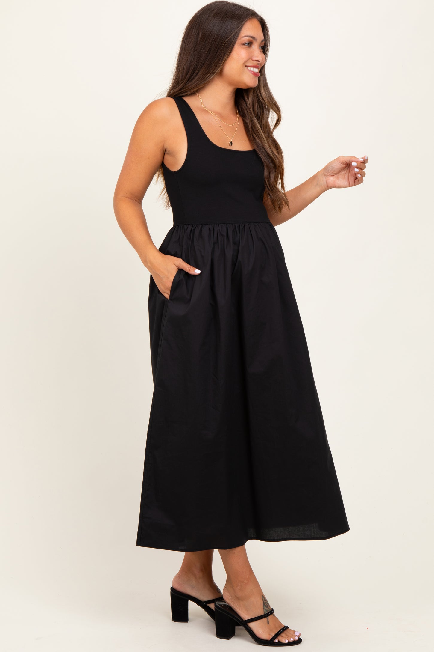 woman wearing a black maternity dress with a fitted top and flowy skirt, featuring side pockets