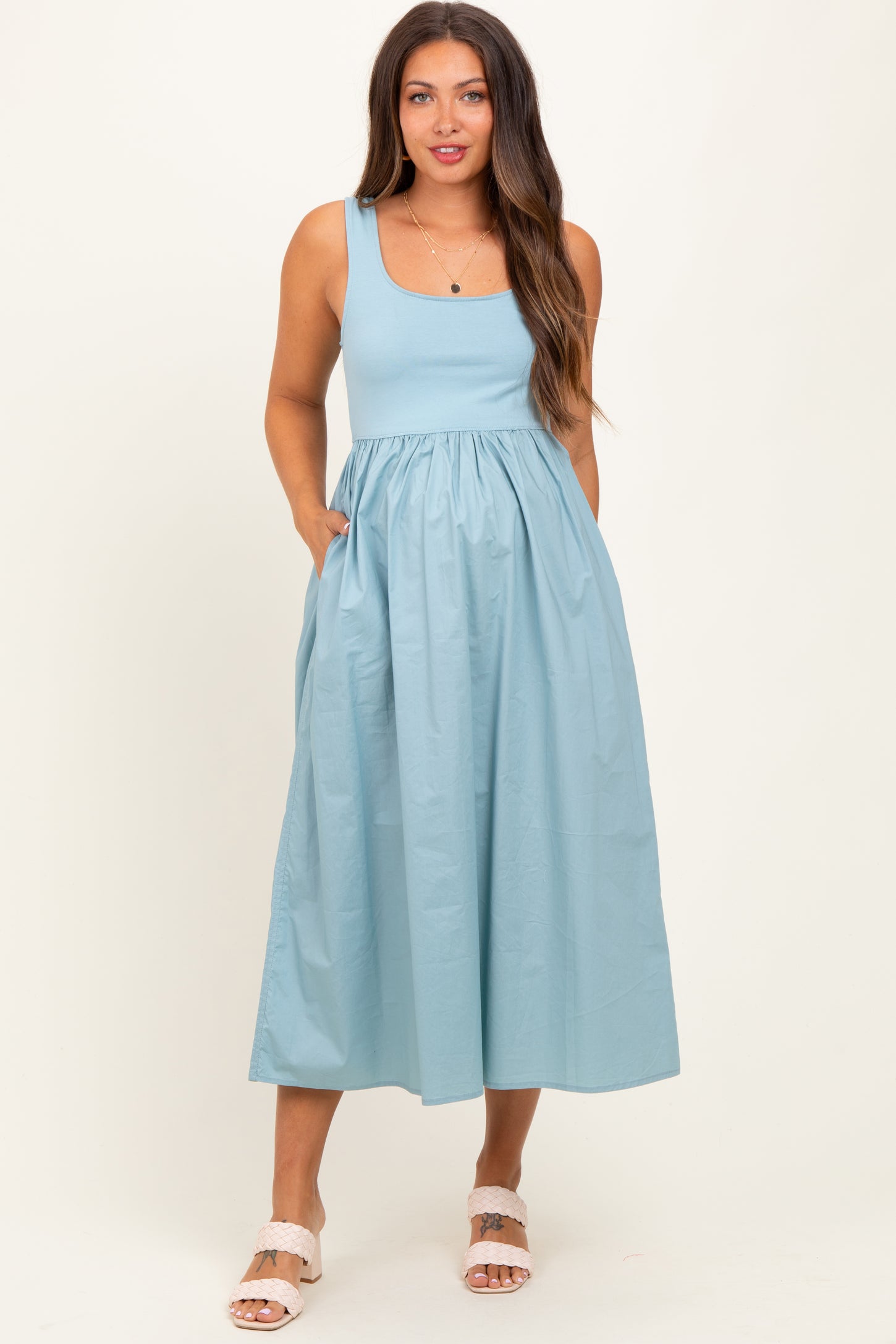 woman wearing a light blue maternity dress with a fitted bodice and full skirt, featuring side pockets