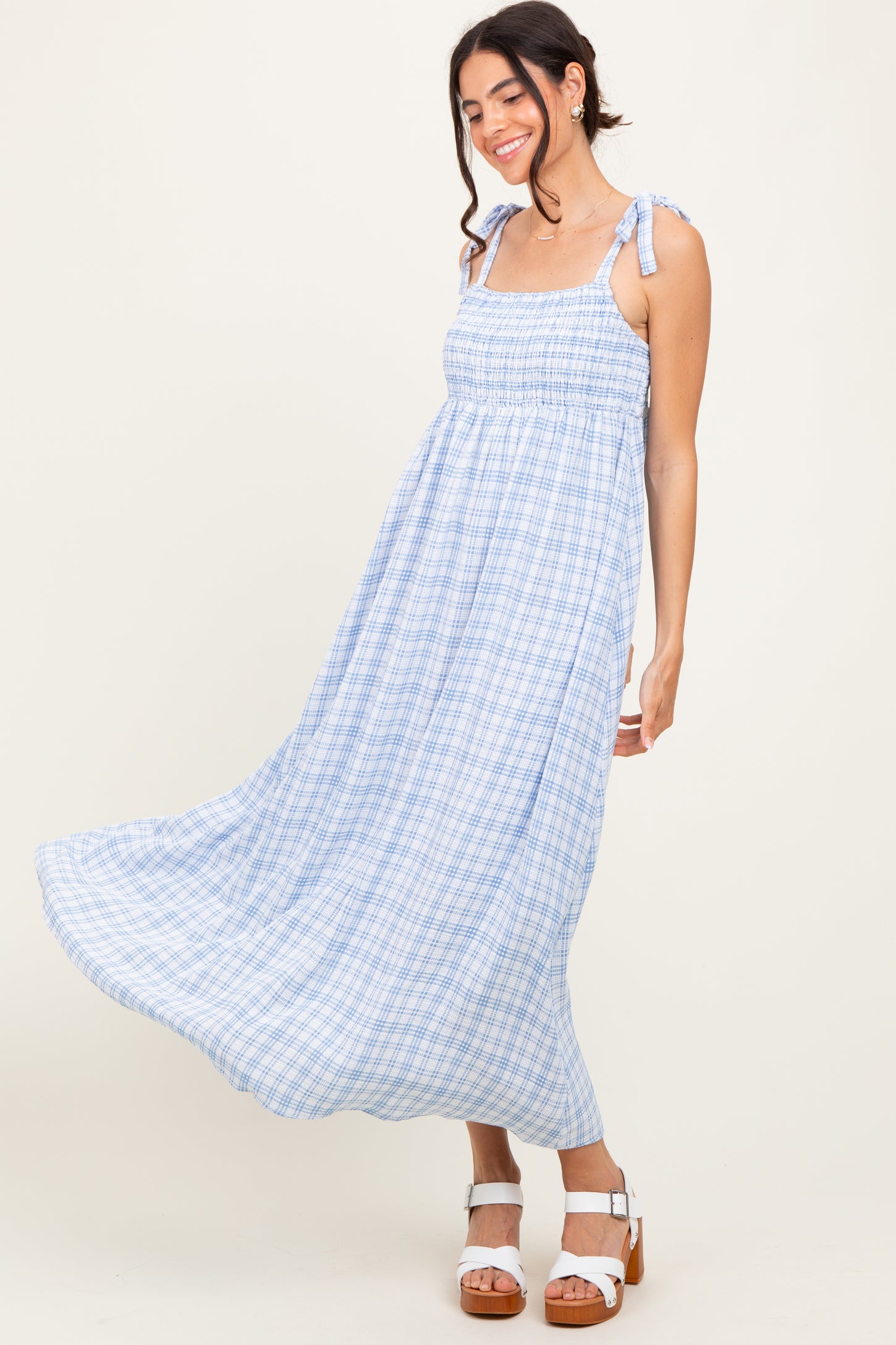 woman wearing a blue and white checkered maxi dress with tie straps, twirling elegantly