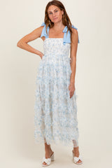 woman wearing a blue floral maxi dress with ruffle details and bow straps, styled with white slide sandals