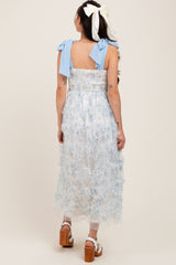 woman wearing a light blue floral maternity dress with smocked bodice and tied shoulder straps, view from the back