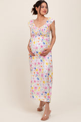 woman wearing a floral maternity maxi dress with ruffled straps, cradling her baby bump