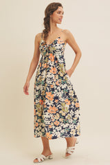 woman wearing a floral midi dress with a knotted front and adjustable spaghetti straps, styled with white sandals