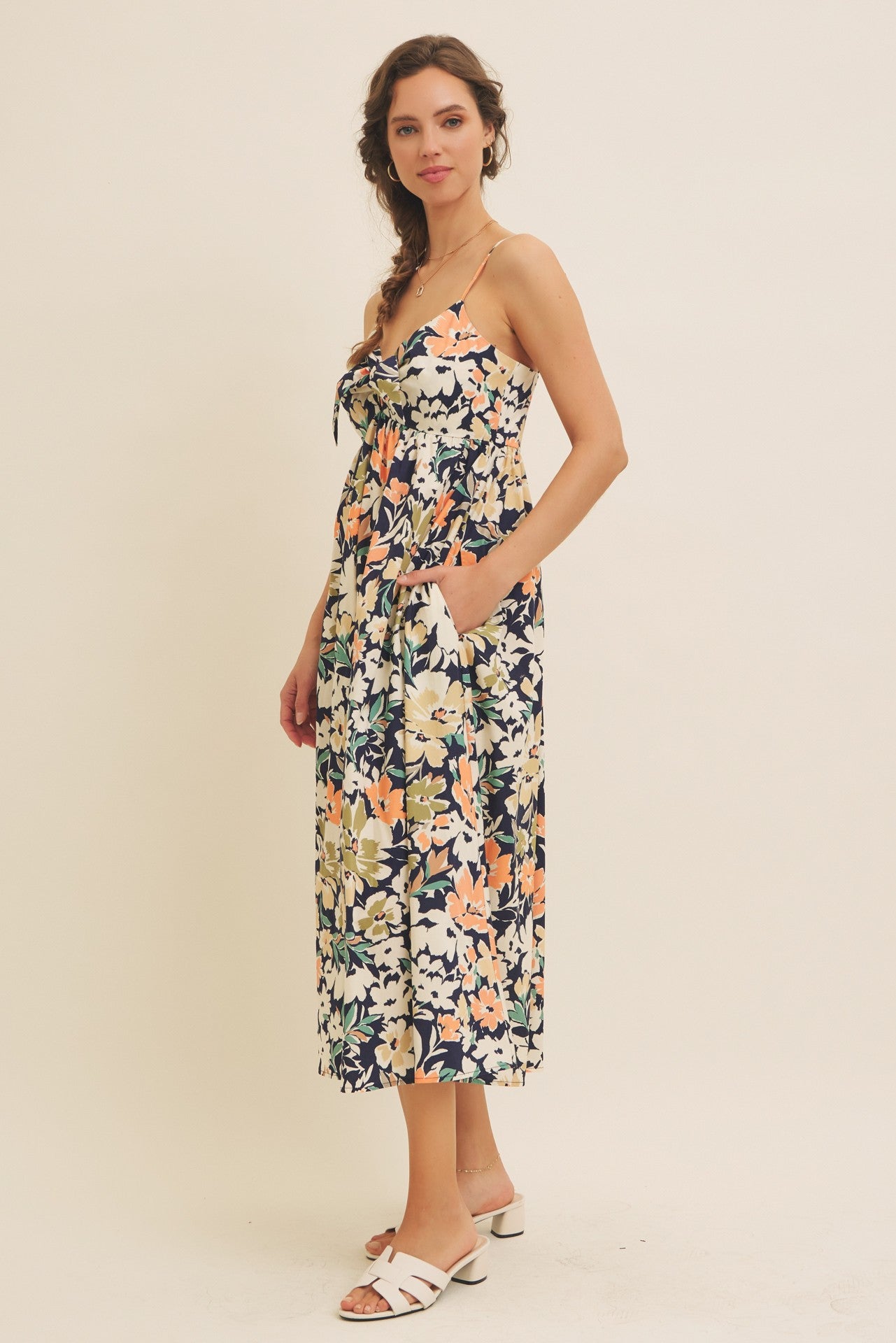 woman wearing a floral midi dress with a tied front and pockets, paired with white sandals