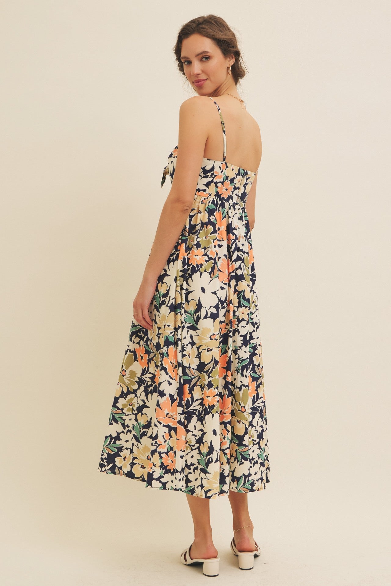 woman wearing a navy blue floral midi dress with adjustable straps and a tie at the back