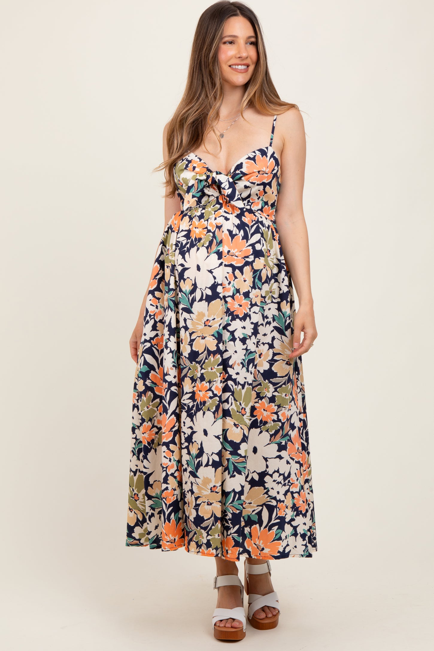 woman wearing a navy floral maternity maxi dress with a tie front and spaghetti straps, showcasing her baby bump