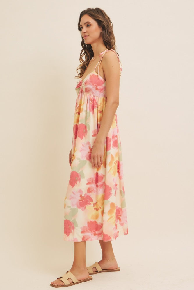 woman wearing a floral maxi dress with pink and yellow hues and tie straps, styled with simple sandals
