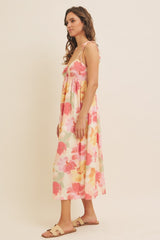 woman wearing a floral maxi dress with pink and yellow hues and tie straps, styled with simple sandals