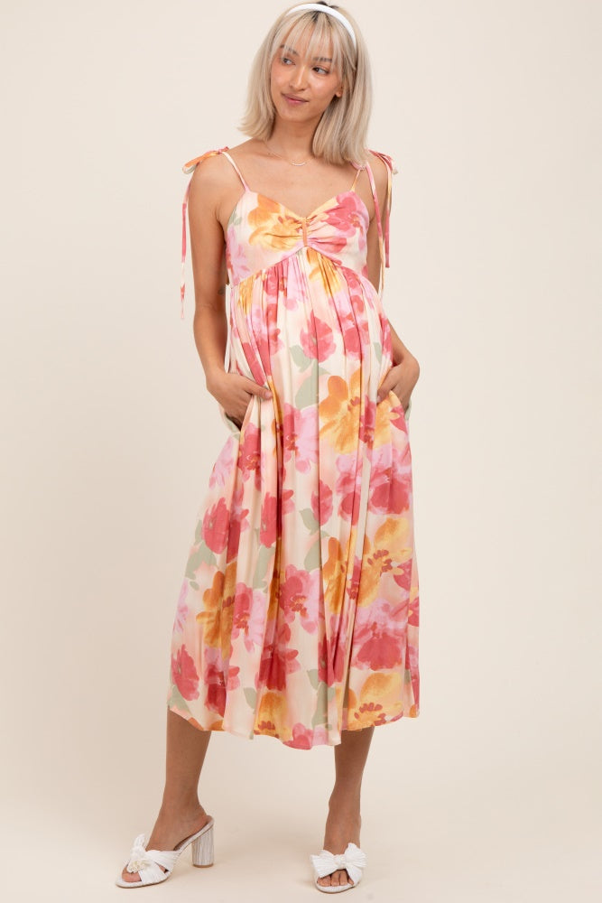 woman wearing a floral maternity dress with adjustable straps, a gathered waist, and pockets, showcasing her baby bump