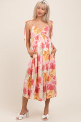 woman wearing a floral maternity dress with adjustable straps, a gathered waist, and pockets, showcasing her baby bump