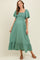 woman wearing a green maternity maxi dress with a square neckline and short puff sleeves, standing in a relaxed pose