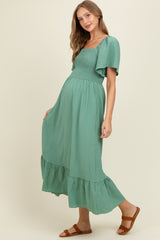 woman wearing a sage green maternity maxi dress with a square neckline and tiered ruffle hem
