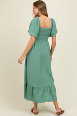 woman wearing a green puff sleeve maternity dress with a square neckline and tiered skirt