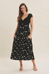 woman wearing a black floral midi dress with a crochet top and pockets, standing against a neutral background