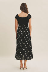 woman wearing a black floral midi dress with a knit bodice and short sleeves, viewed from the back
