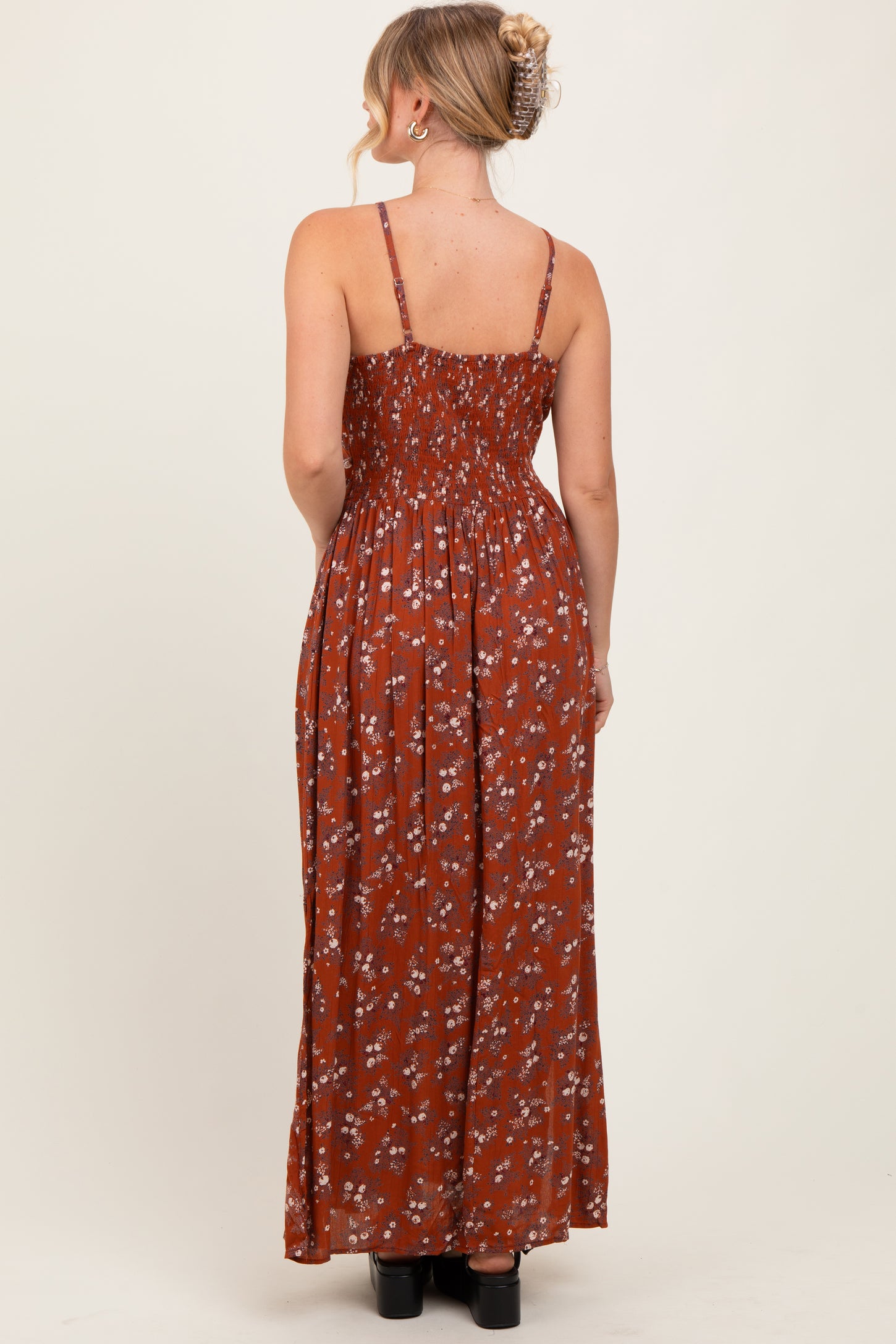 woman wearing a back view of a rust-colored floral maxi dress with adjustable straps and a smocked bodice