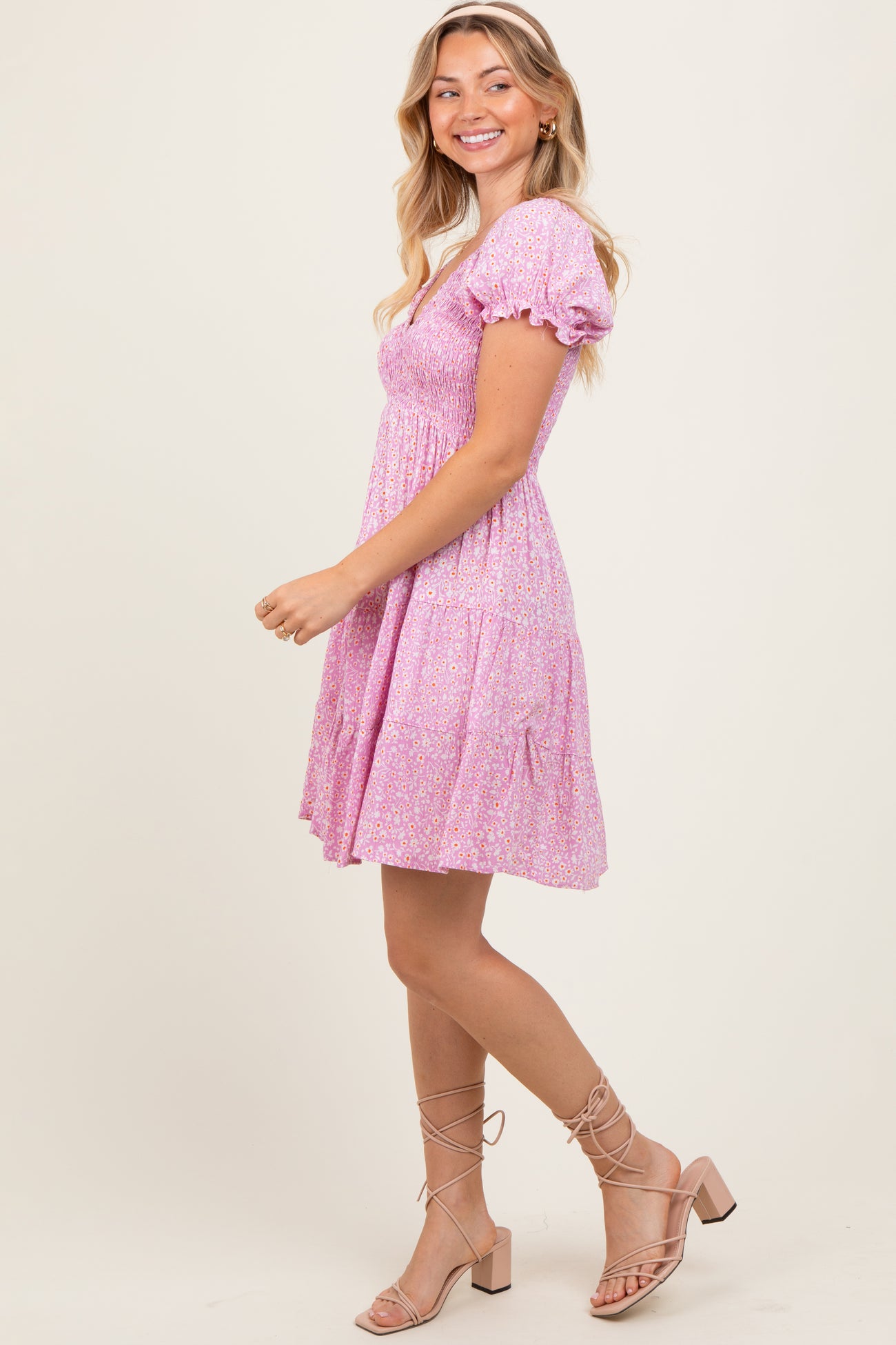 woman wearing a pink floral puff sleeve mini dress and beige strappy sandals, smiling and posing sideways