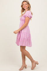 woman wearing a pink floral puff sleeve mini dress and beige strappy sandals, smiling and posing sideways