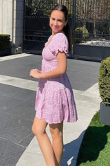 woman wearing a pink floral short sleeve dress, smiling while standing outdoors
