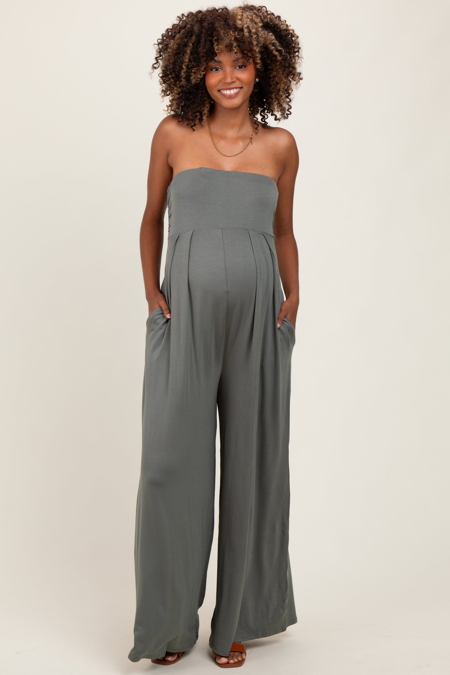 woman wearing a green strapless maternity jumpsuit with wide legs and pockets, showing her baby bump