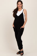 woman wearing a black maternity jumpsuit with adjustable straps and pockets, showcasing her baby bump