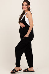 woman wearing a black maternity jumpsuit with a white tank top underneath and showing her baby bump