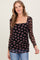 woman wearing a black sheer long sleeve top with floral print and ruched detailing, styled with blue jeans