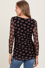 woman wearing a black long sleeve top with floral print and sheer sleeves, showing a ruched back detail