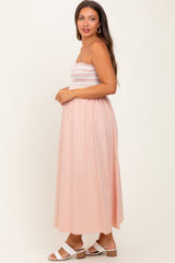 woman wearing a light pink maternity maxi dress with a smocked bodice and a flowing skirt, showing her baby bump