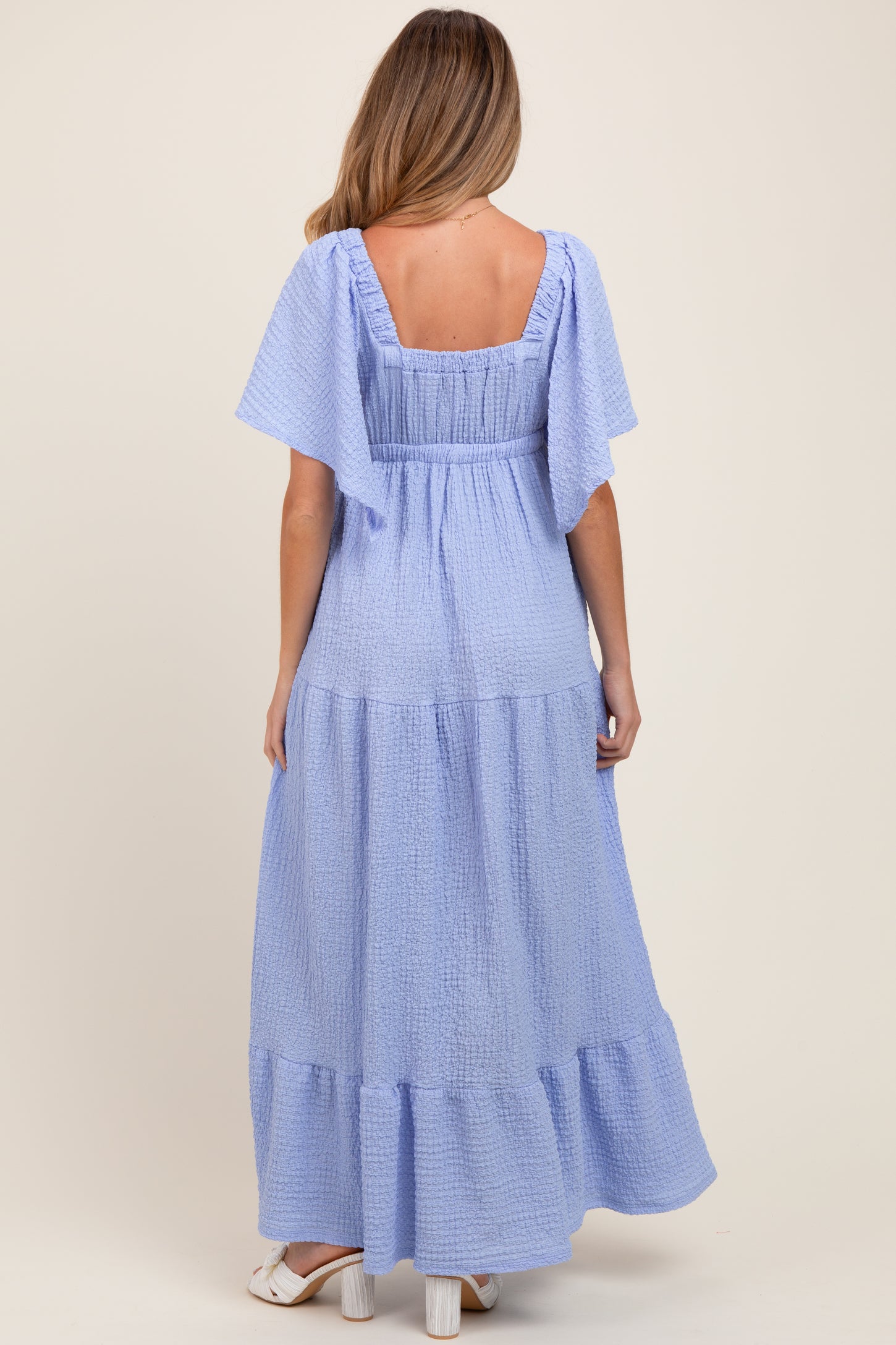 woman wearing a light blue maternity maxi dress with short flutter sleeves and tiered hem from the back