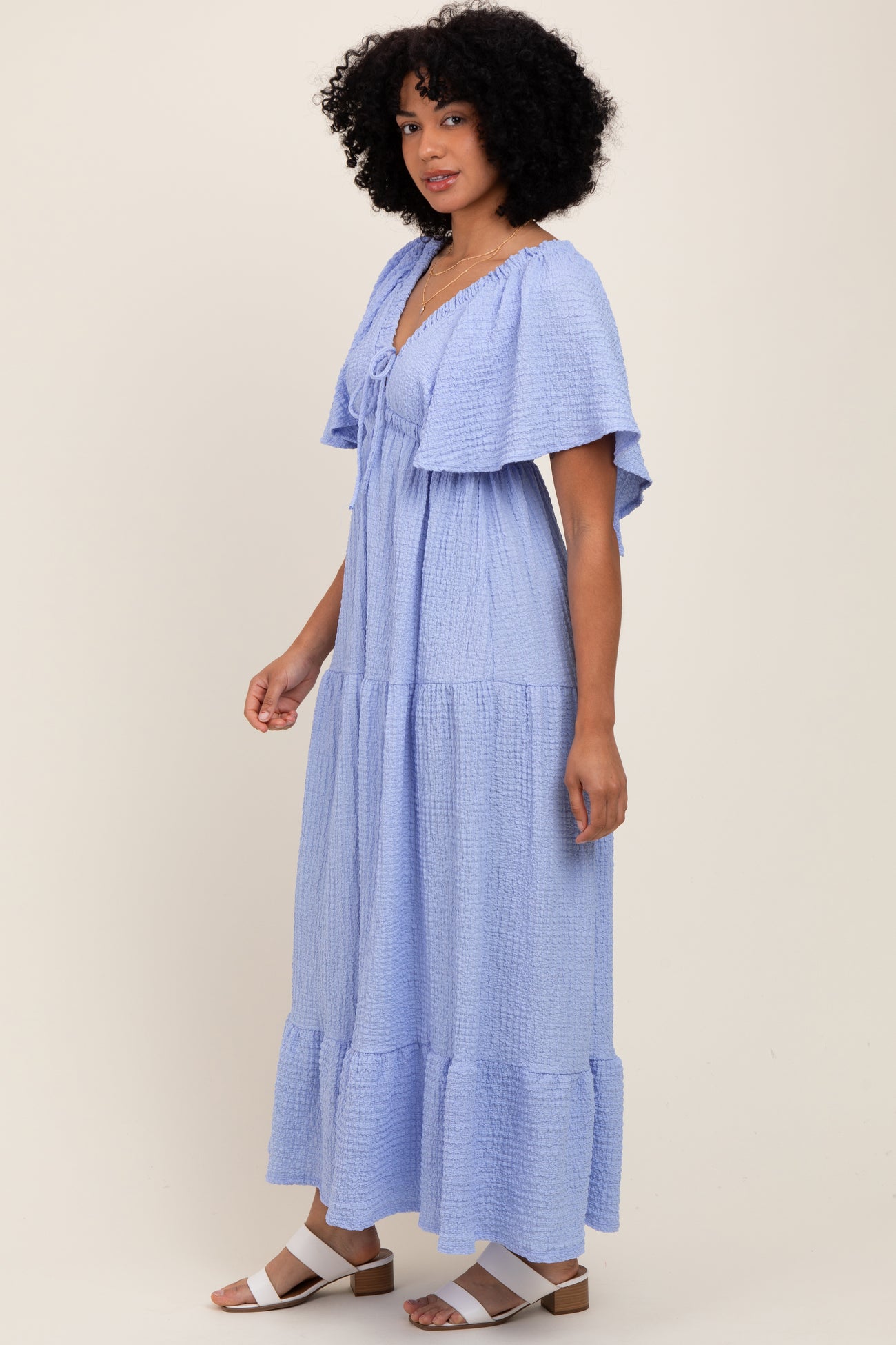 woman wearing a light blue maxi dress with short flutter sleeves and button detail, standing against a neutral background
