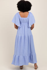 woman wearing a light blue tiered maxi dress with flutter sleeves and a smocked waist, shown from the back