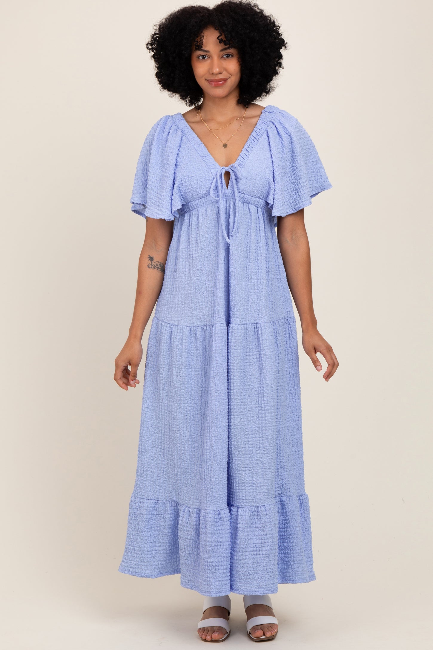 woman wearing a light purple tiered maxi dress with short flutter sleeves and a tie detailing at the neckline