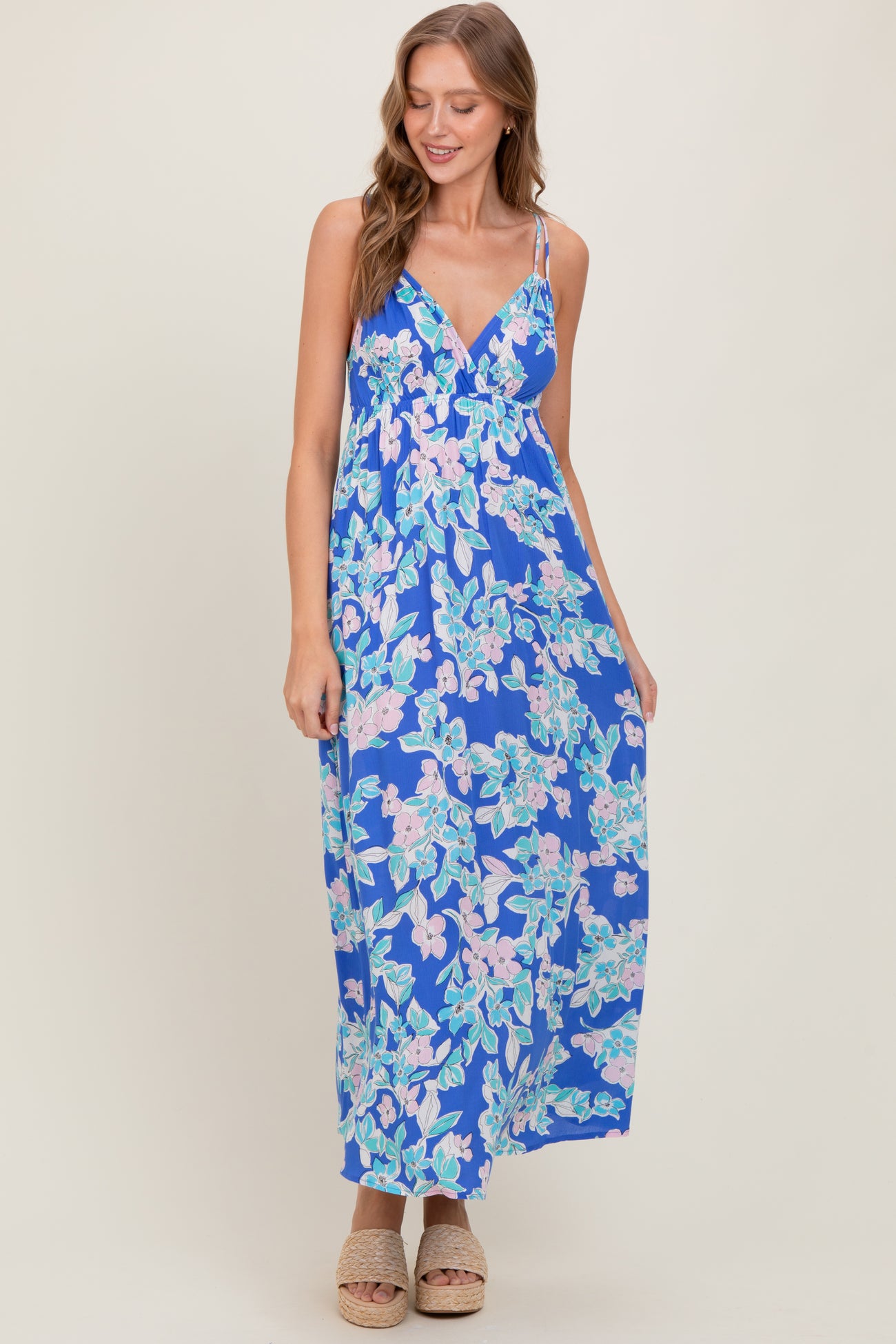 woman wearing a blue floral maxi dress with a v-neckline and spaghetti straps, standing and smiling