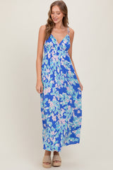 woman wearing a blue floral maxi dress with a v-neckline and spaghetti straps, standing and smiling