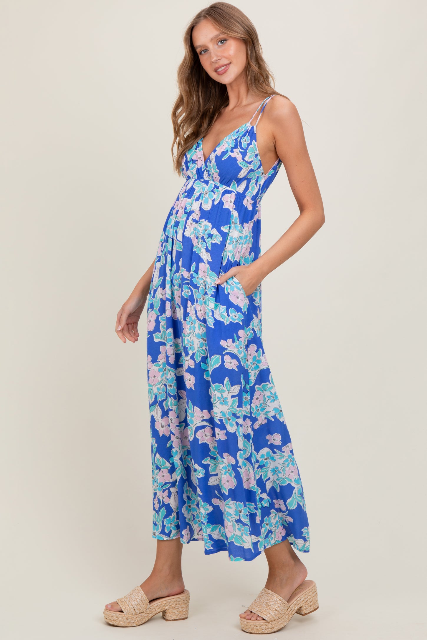 woman wearing a blue floral maxi dress with a deep v-neckline and pockets, standing on a light background