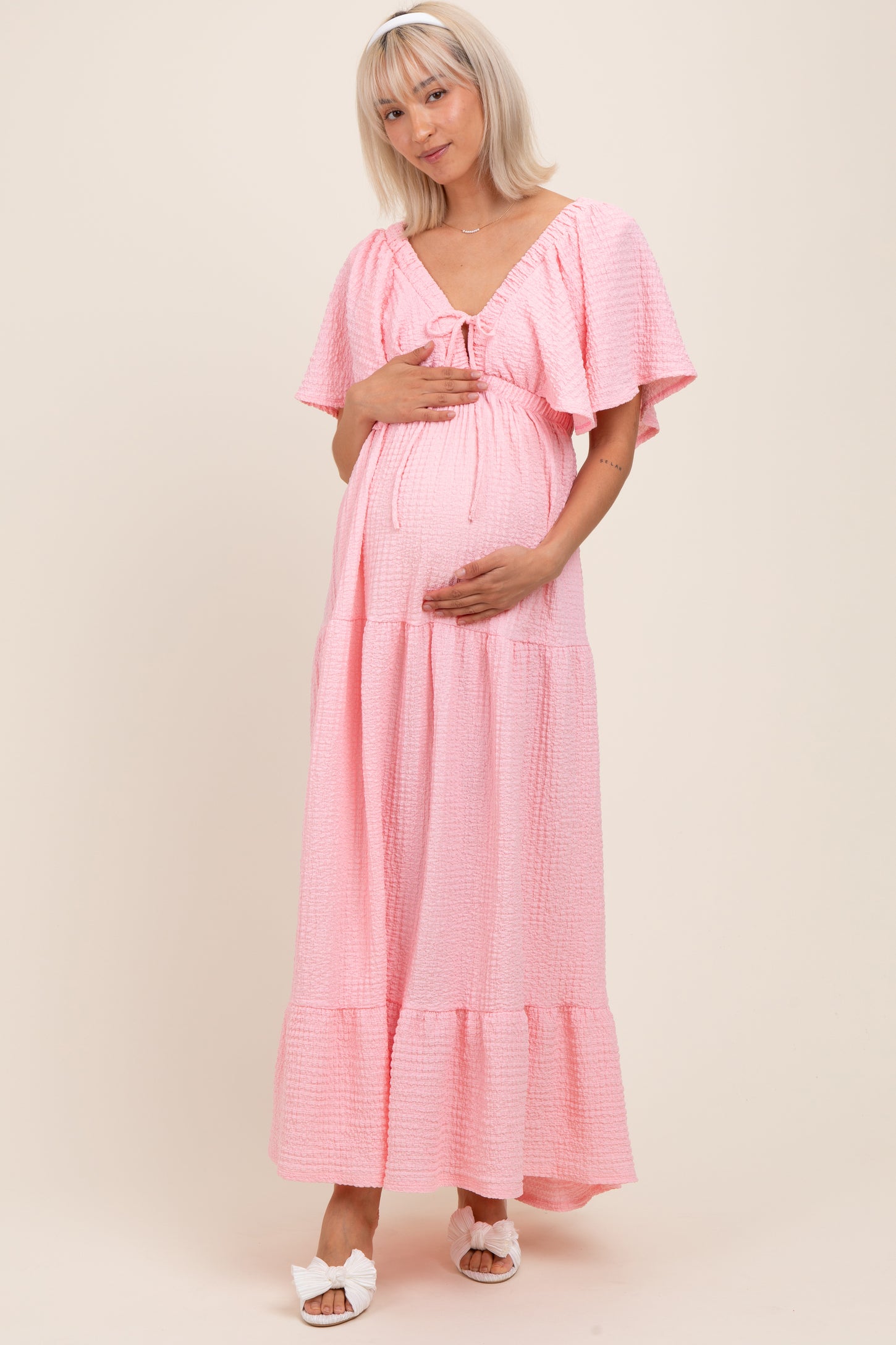 woman wearing a pink short sleeve maternity dress with a tie front and holding her baby bump