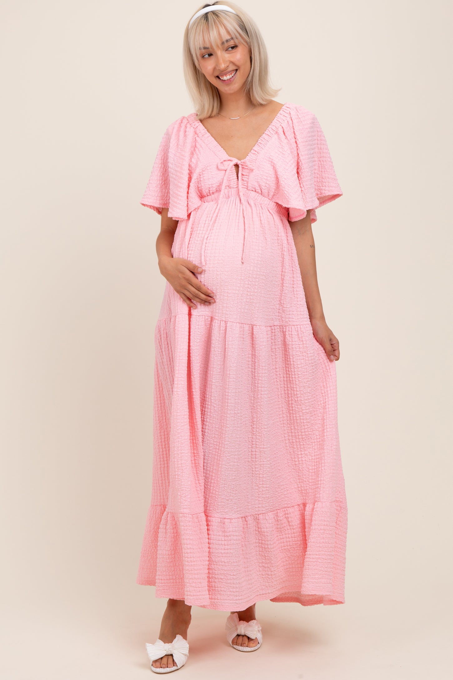 woman wearing a pink puff sleeve maternity maxi dress and holding her baby bump